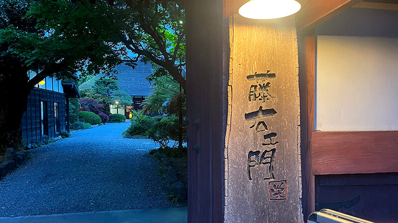 藤右ェ門 栄の看板と青く暮れた庭へ続く玉砂利の道