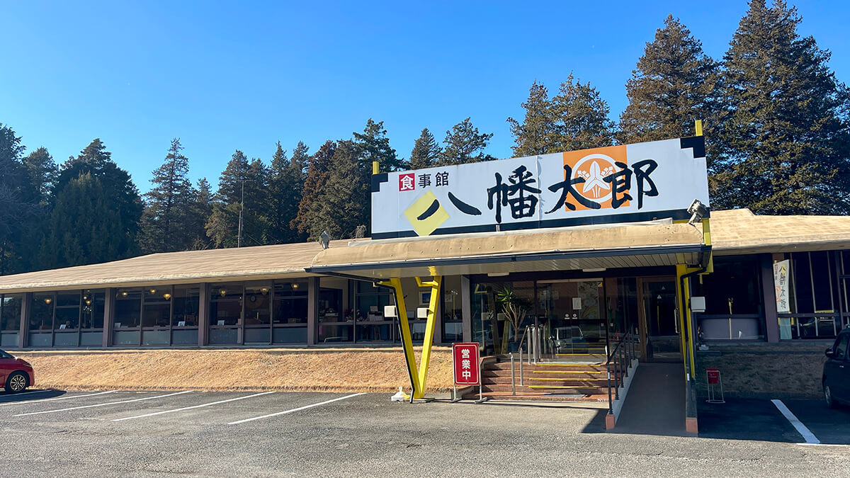 青空の下に立つ食事館 八幡太郎の看板と店舗外観