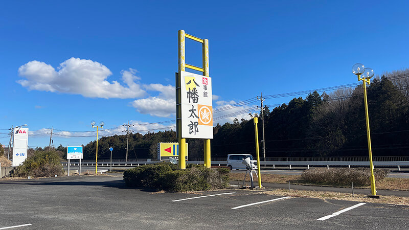 青空の下に立つ食事館 八幡太郎の大きな道路沿い看板