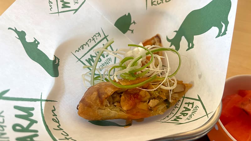 白ねぎとソースをのせて店名入りの紙に置かれたGINGER FARM KITCHENの春巻き