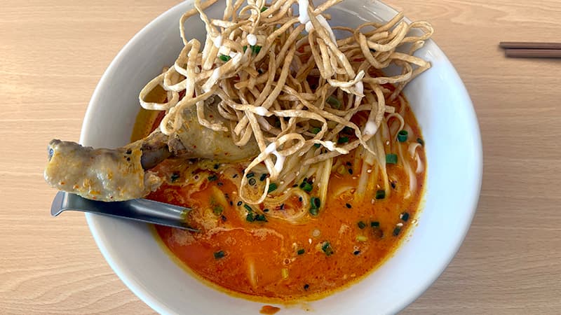 揚げ麺をのせ骨付き鶏もも肉が入ったGINGER FARM KITCHENのカオソーイガイ