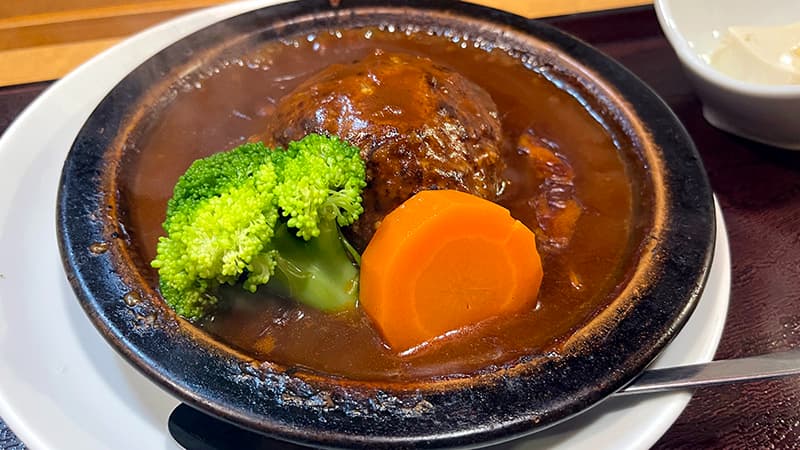 濃い煮込みソースに包まれた大きなハンバーグ