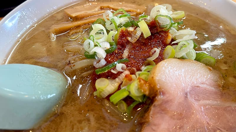 ねぎの下に隠れたあおり辛味噌ラーメンの赤い辛味噌ダレのアップ