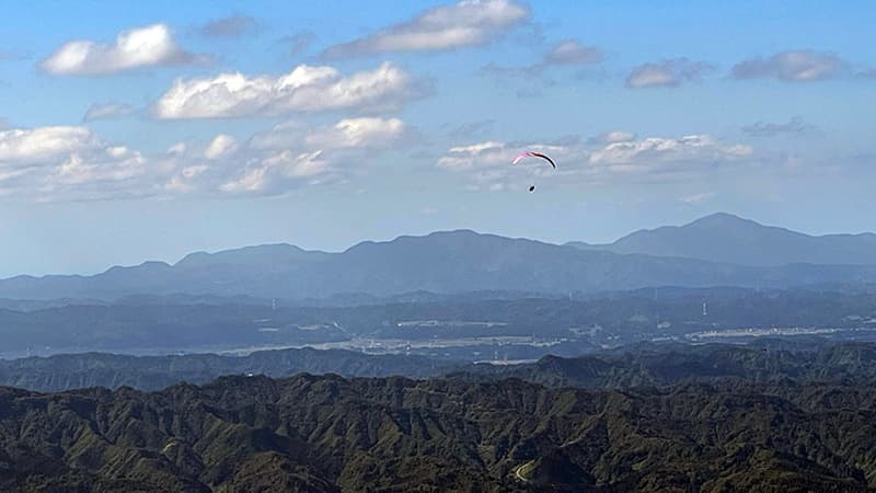 八海山の上空を飛ぶパラグライダーと遠くまで重なる山の稜線